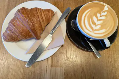 A butter croissant on a white plate beside a cup of coffee