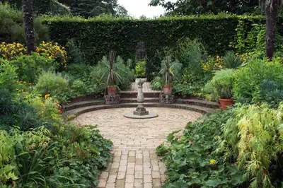 A brick path through deep planted borders to a round terrace with a sundial