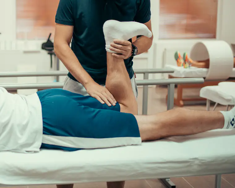A physiotherapist bends a patient’s knee to stretch his thigh as he lies on a treatment couch