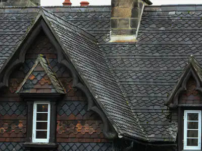 A slate roof with two gabled dormer windows and patterned slate hanging