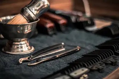 A shaving brush in a steel bowl beside cut-throat razors and clipper guards