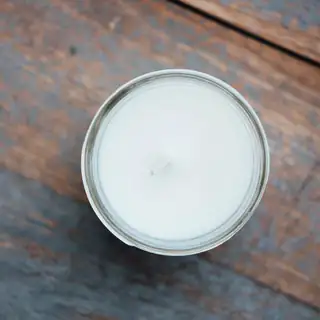 A white soy candle seen from above in a round tin on weathered wood