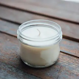 A small glass jar of white soy candle on a wooden table